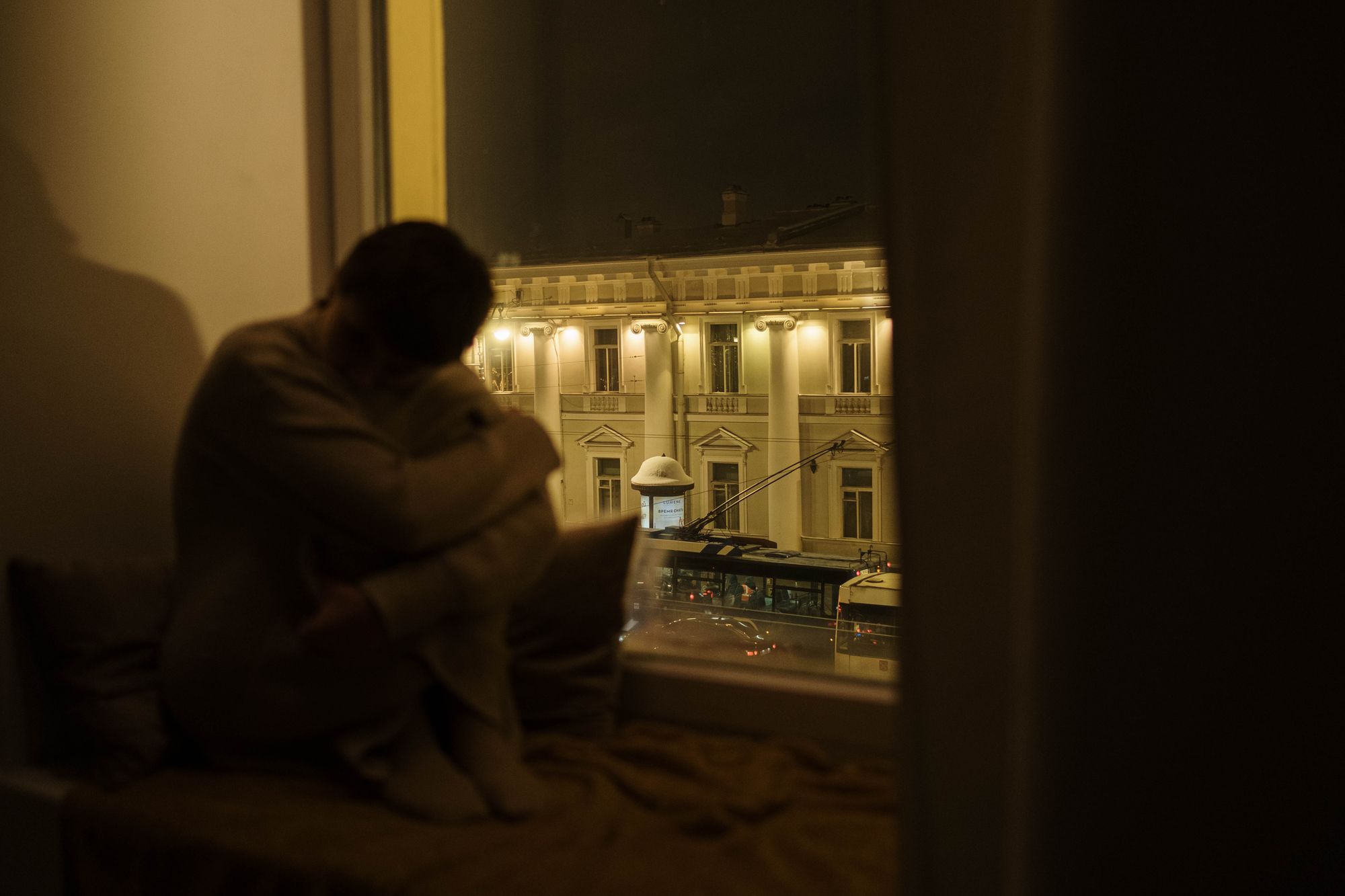 Someone alone by the window at night, phone in hand